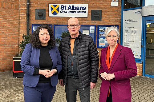 Victoria, Paul and Daisy (from left to right) are standing in front of the St Albans District Council building. They have serious expressions.