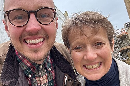 Adam Dance MP smiles for a selfie with Police and Crime Commissioner Clare Moody outdoors on a cloudy day, with buildings and scaffolding in the background