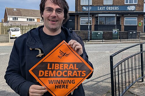 Paul Edgeworth standing holding a Liberal Democrats 'Winning Here' sign