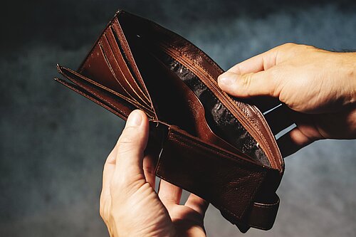 A person opening a wallet to reveal it is empty.
