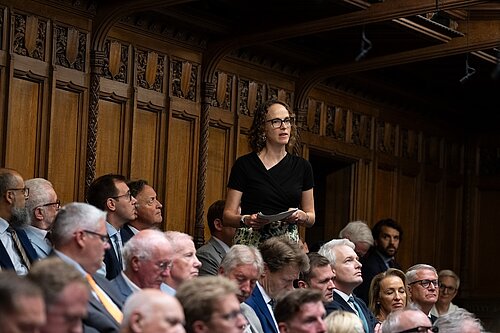 Alison Bennett MP asking a question in the parliamentary chamber, surrounded by sitting MPs