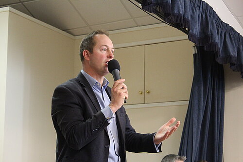 Richard Foord on a stage giving a talk while holding a microphone