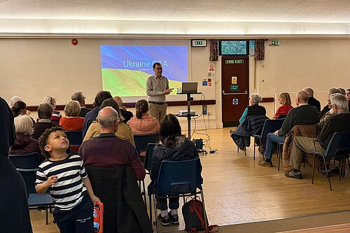 Tom Gordon giving a talk with a powerpoint displaying the Ukraine flag in the background